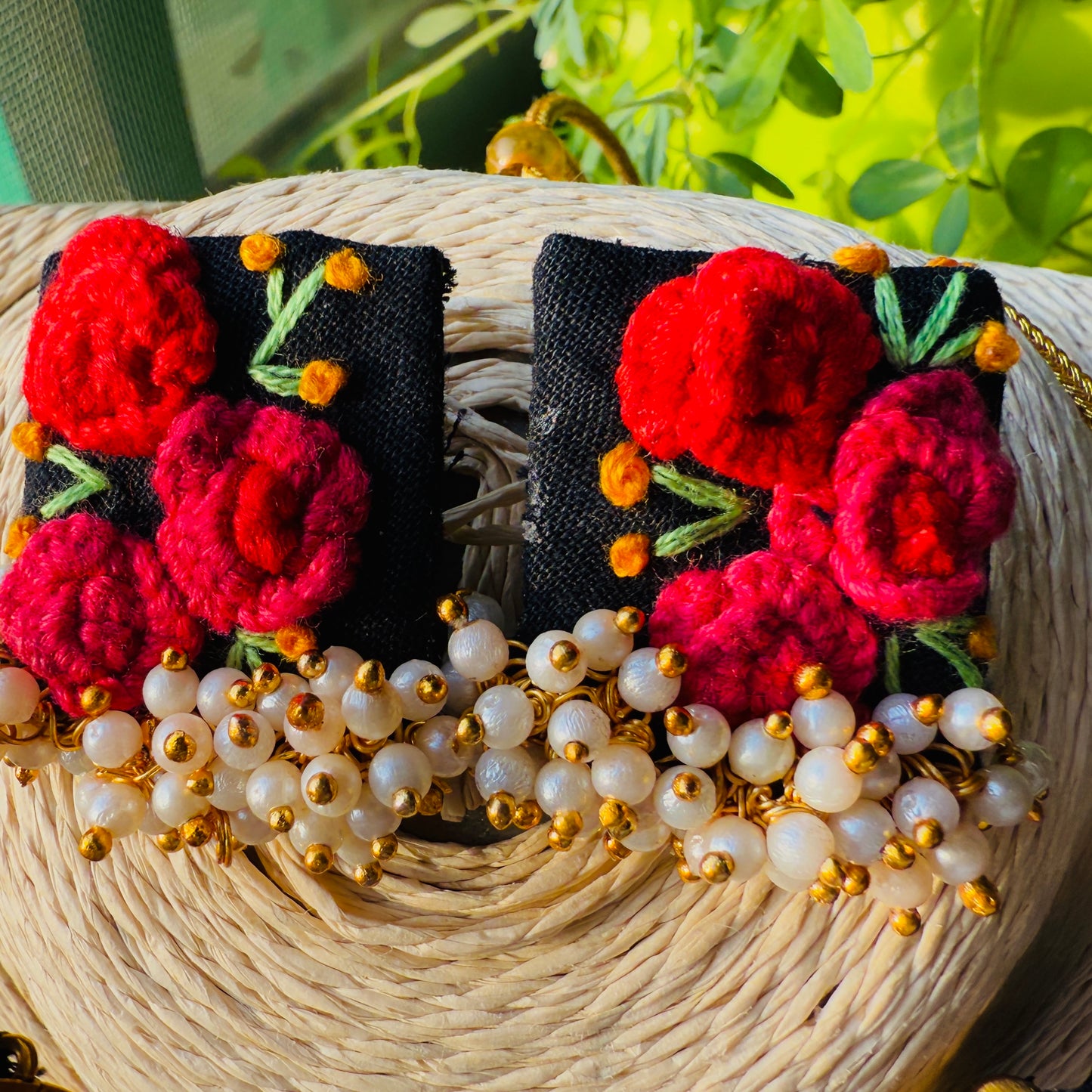 Pair of earrings with red floral designs and pearl-like beads on a woven surface.