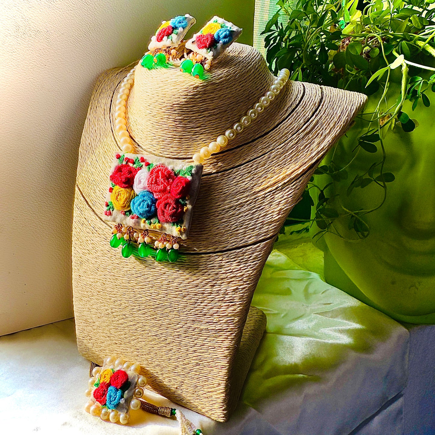 Colorful floral jewelry set on a straw hat with a green plant in the background