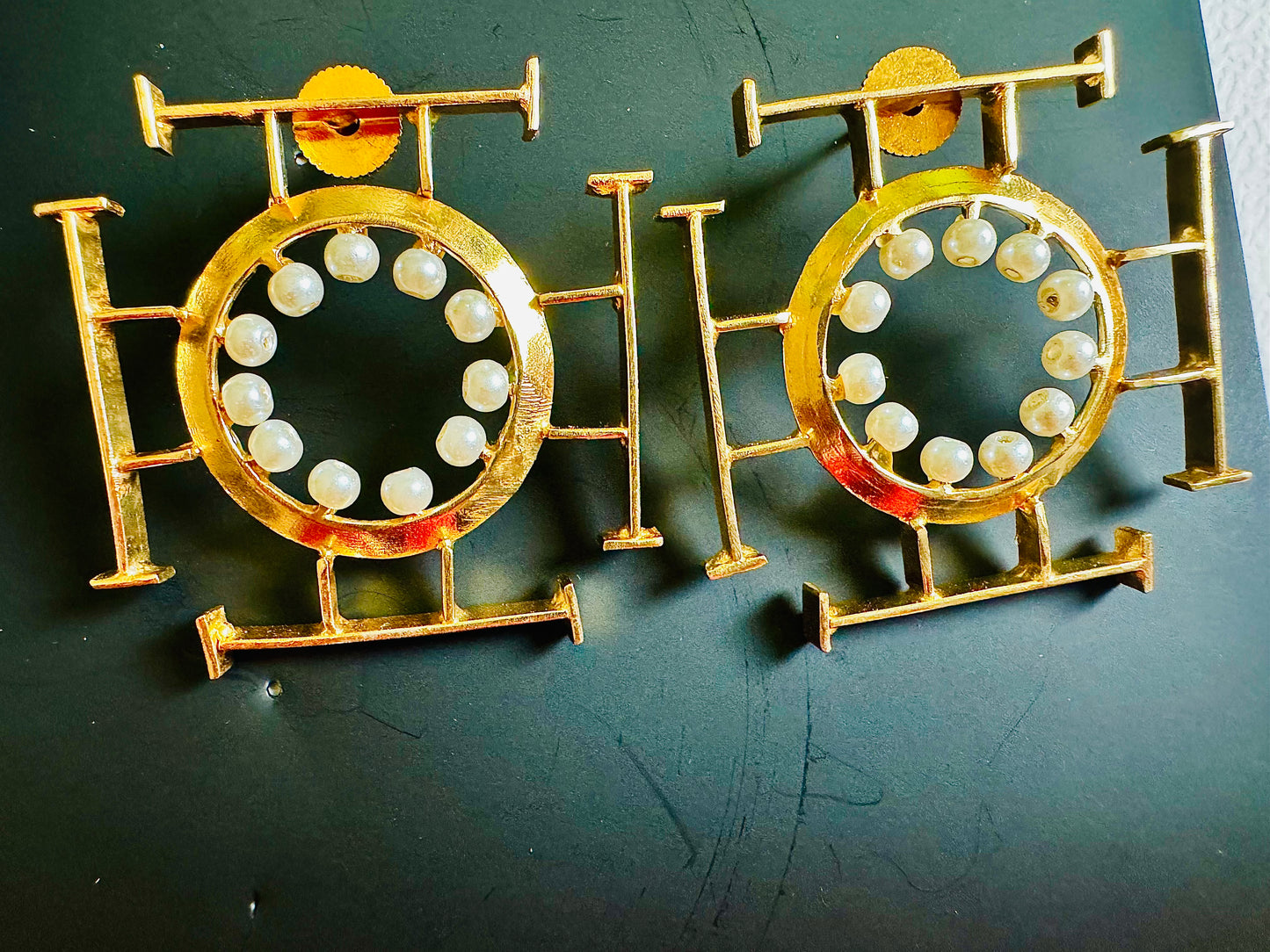 Gold earrings with circular designs and pearl-like beads on a dark background