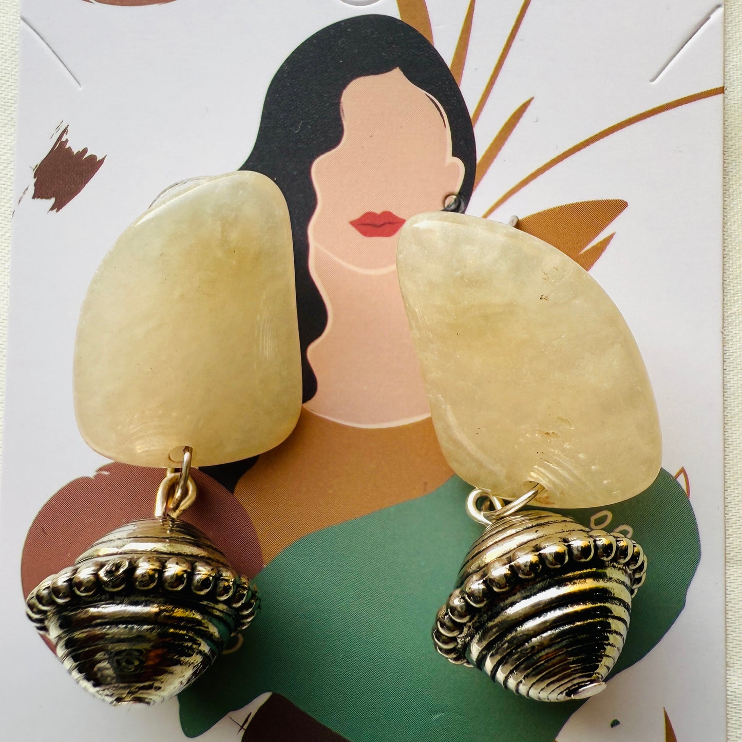 Shell-shaped earrings on a decorative card with a woman's face.