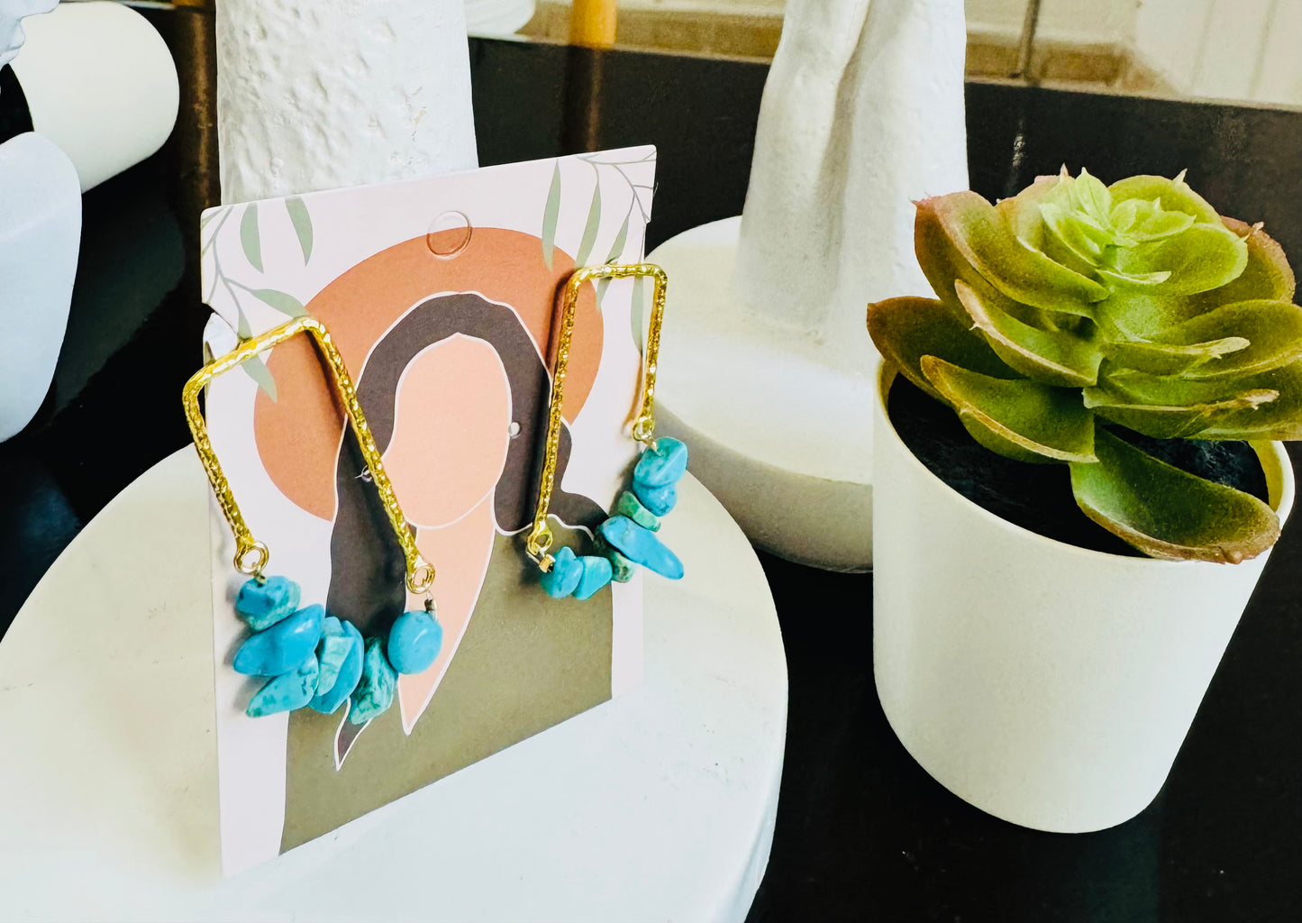 Turquoise earrings on a card with a succulent plant in the background