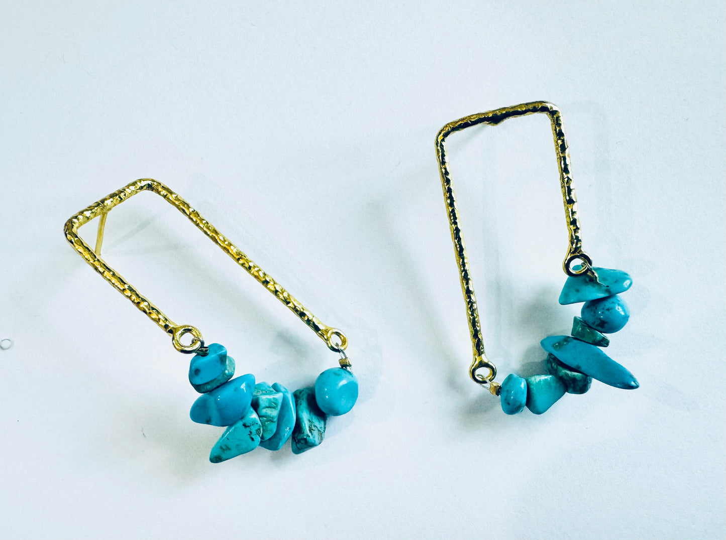 Pair of turquoise stone earrings on gold chains against a white background
