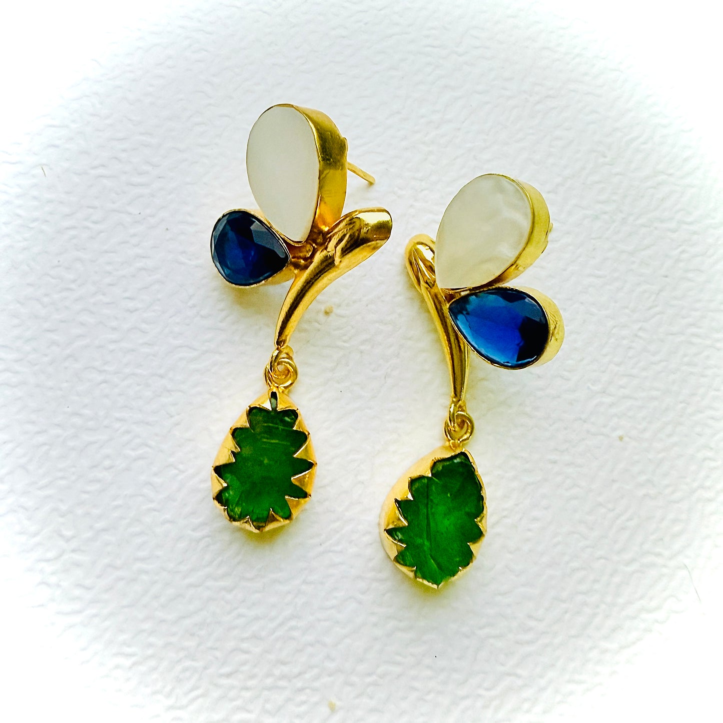 Gold earrings with green and blue gemstones on a white background