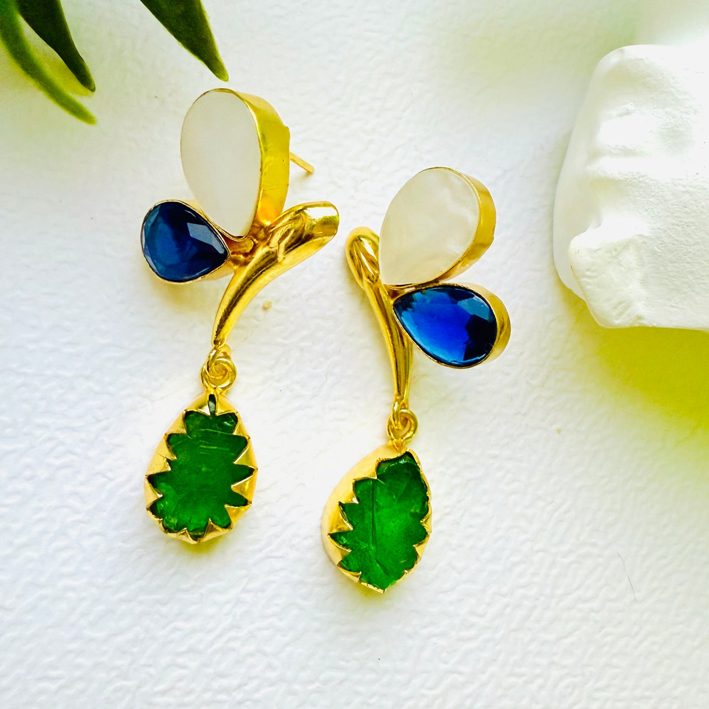 Gold earrings with blue and green stones on a white surface