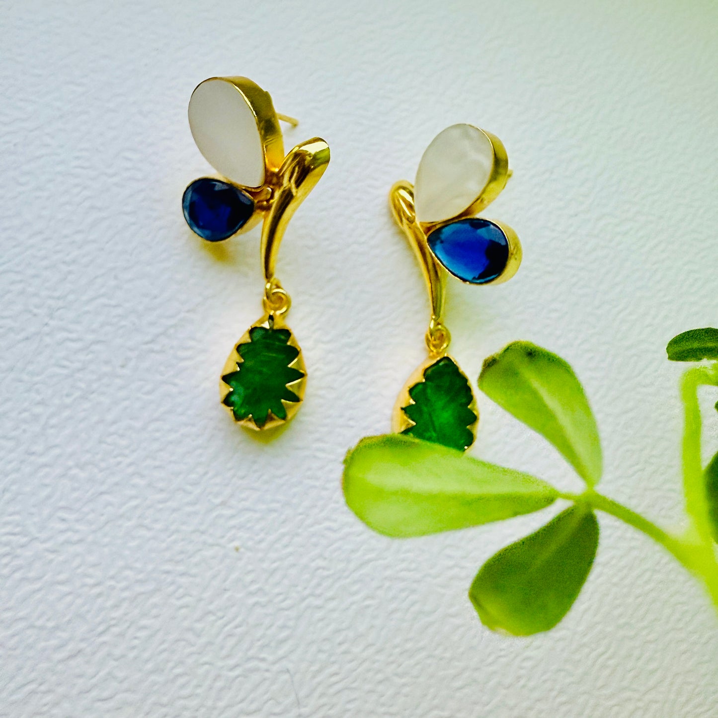 Gold earrings with blue and green stones on a white background with a leaf.