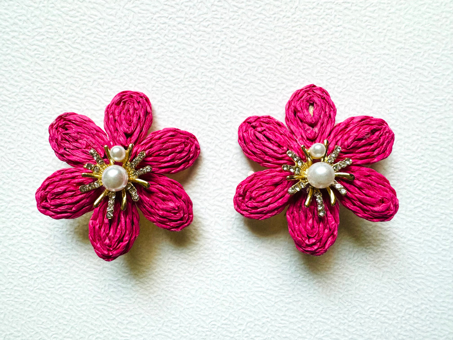 Pair of pink flower-shaped earrings with pearl centers on a white background