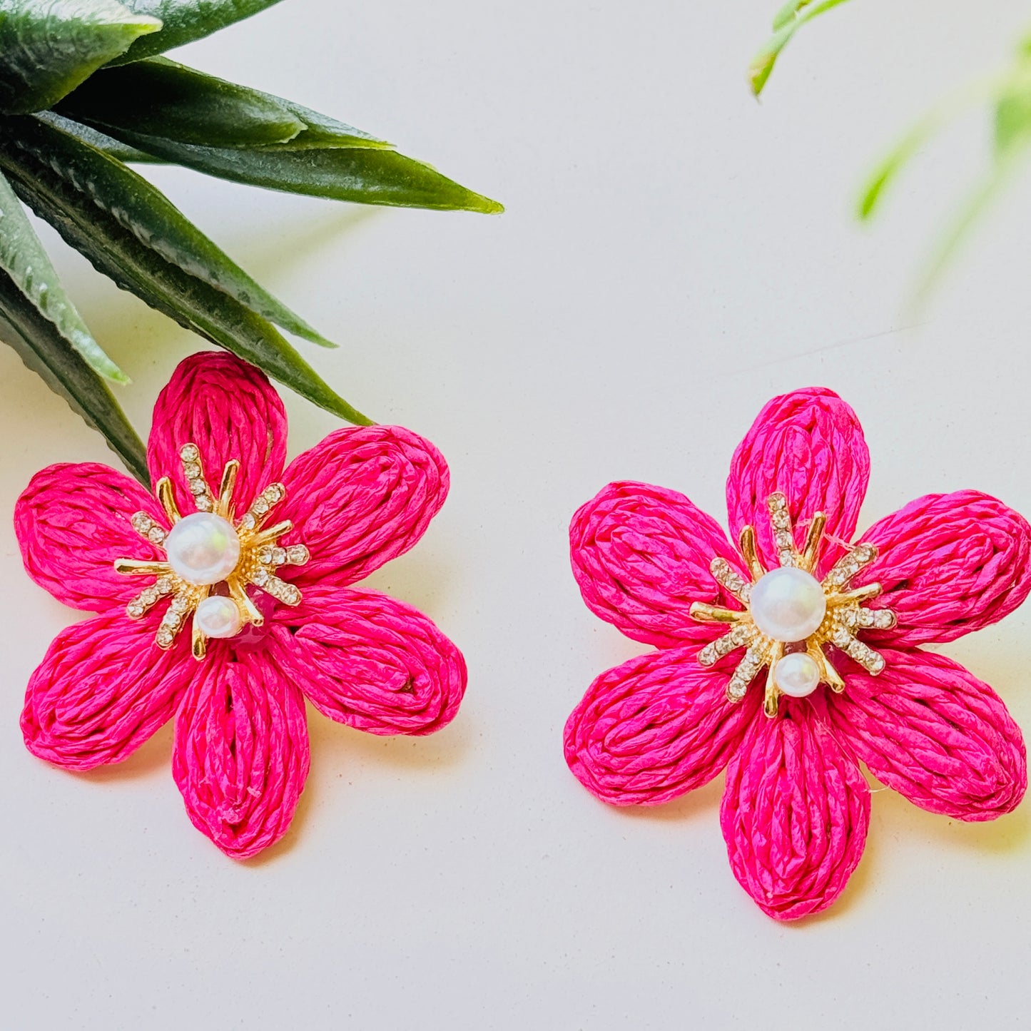Pair of pink flower-shaped earrings with pearl center on a light background
