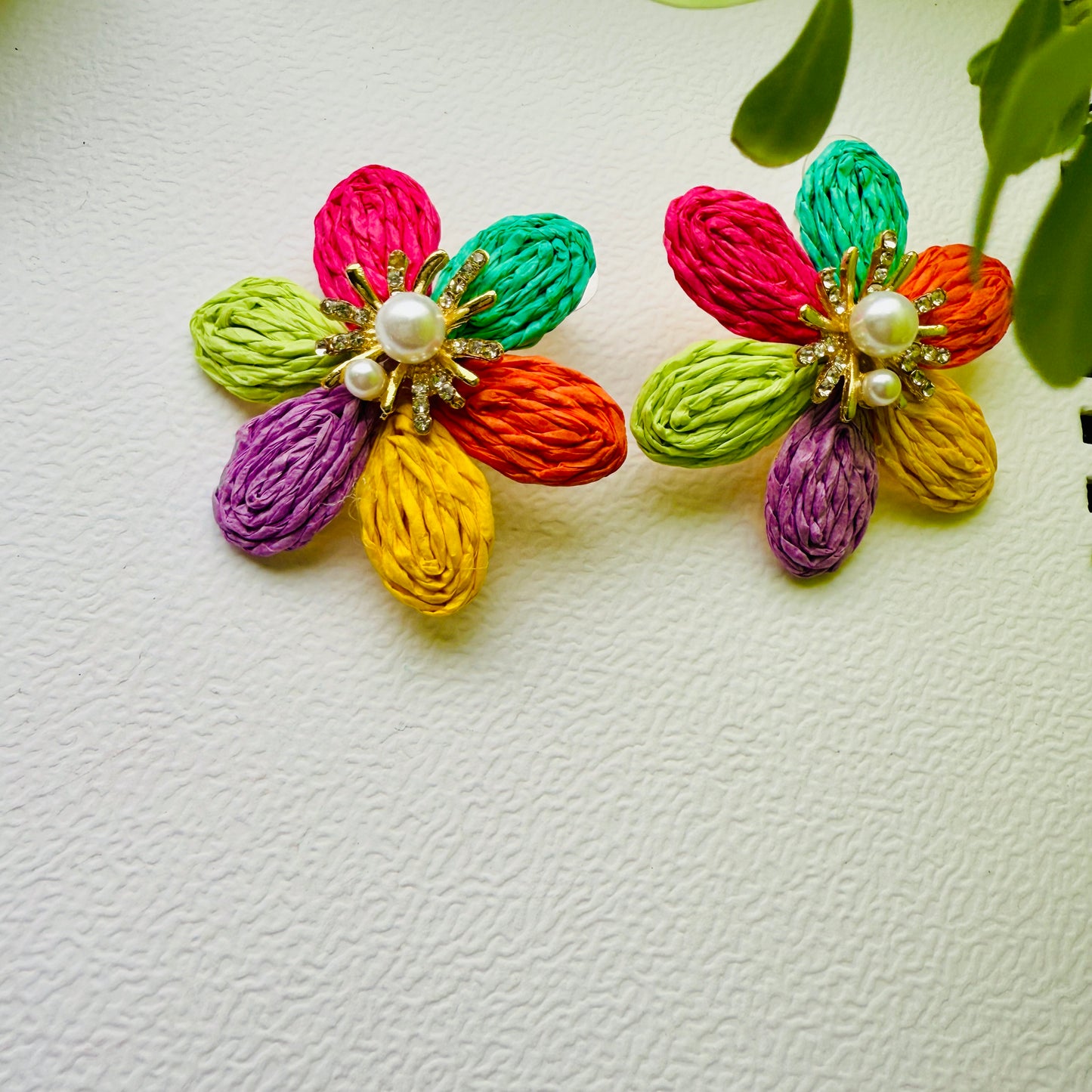 Colorful flower-shaped earrings with pearl centers on a textured white background