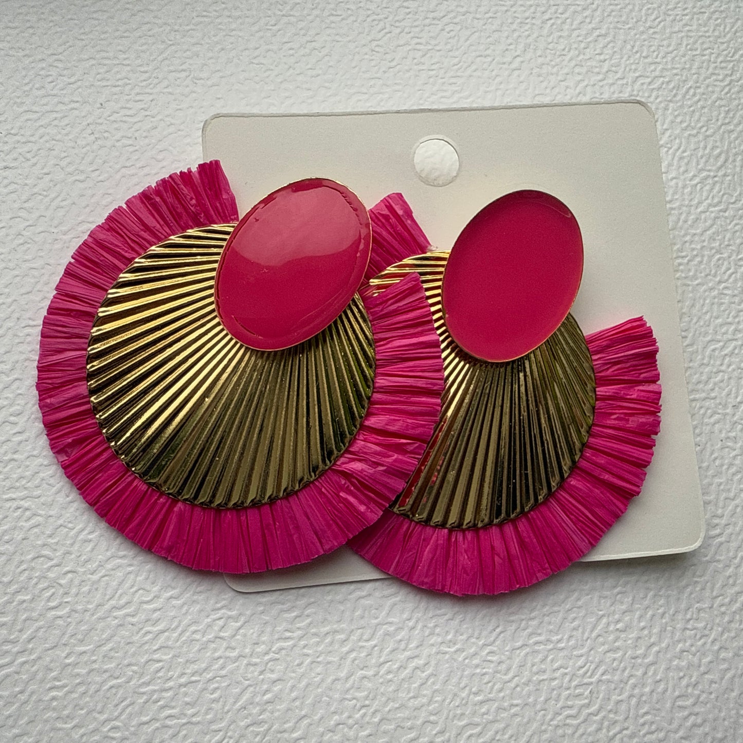 Pair of pink and gold earrings on a white card against a textured white background