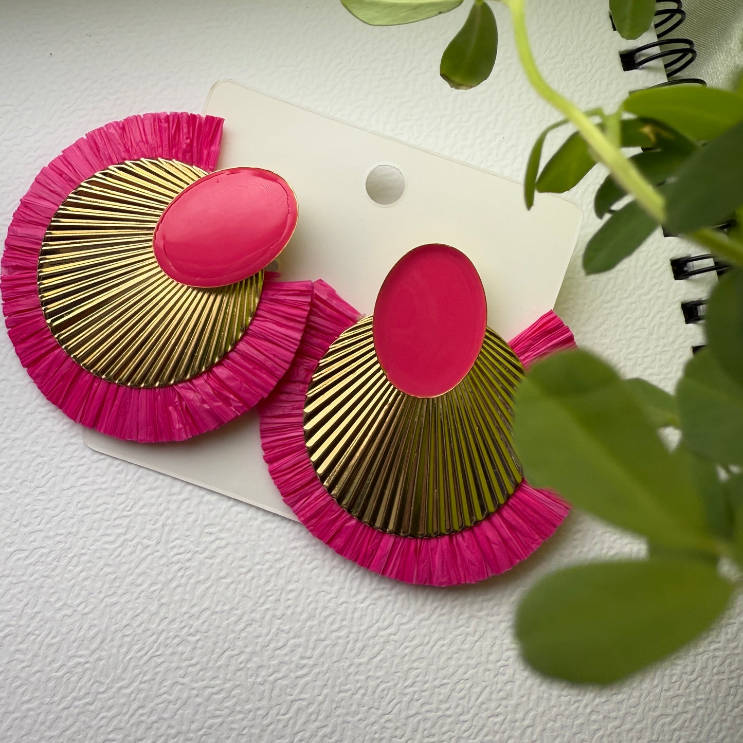 Pink and gold earrings on a white background with green leaves.