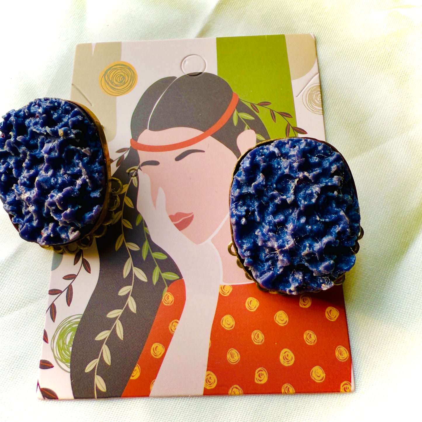 Blue textured earrings on a decorative card with a woman's face