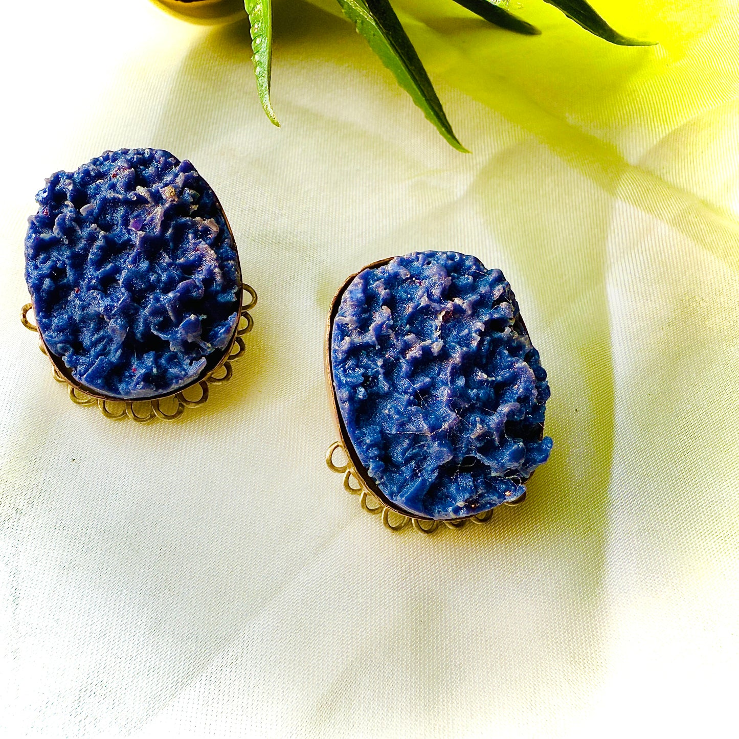 Pair of blue stone earrings on a light yellow fabric background