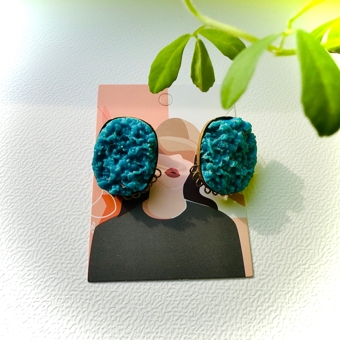 Teal textured earrings on a display card with a light background