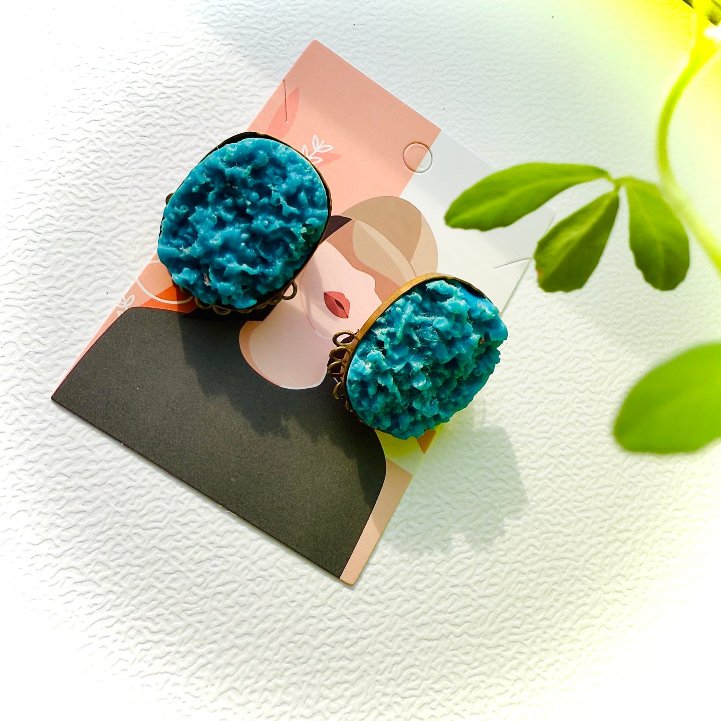 Pair of blue earrings on a display card with a plant in the background