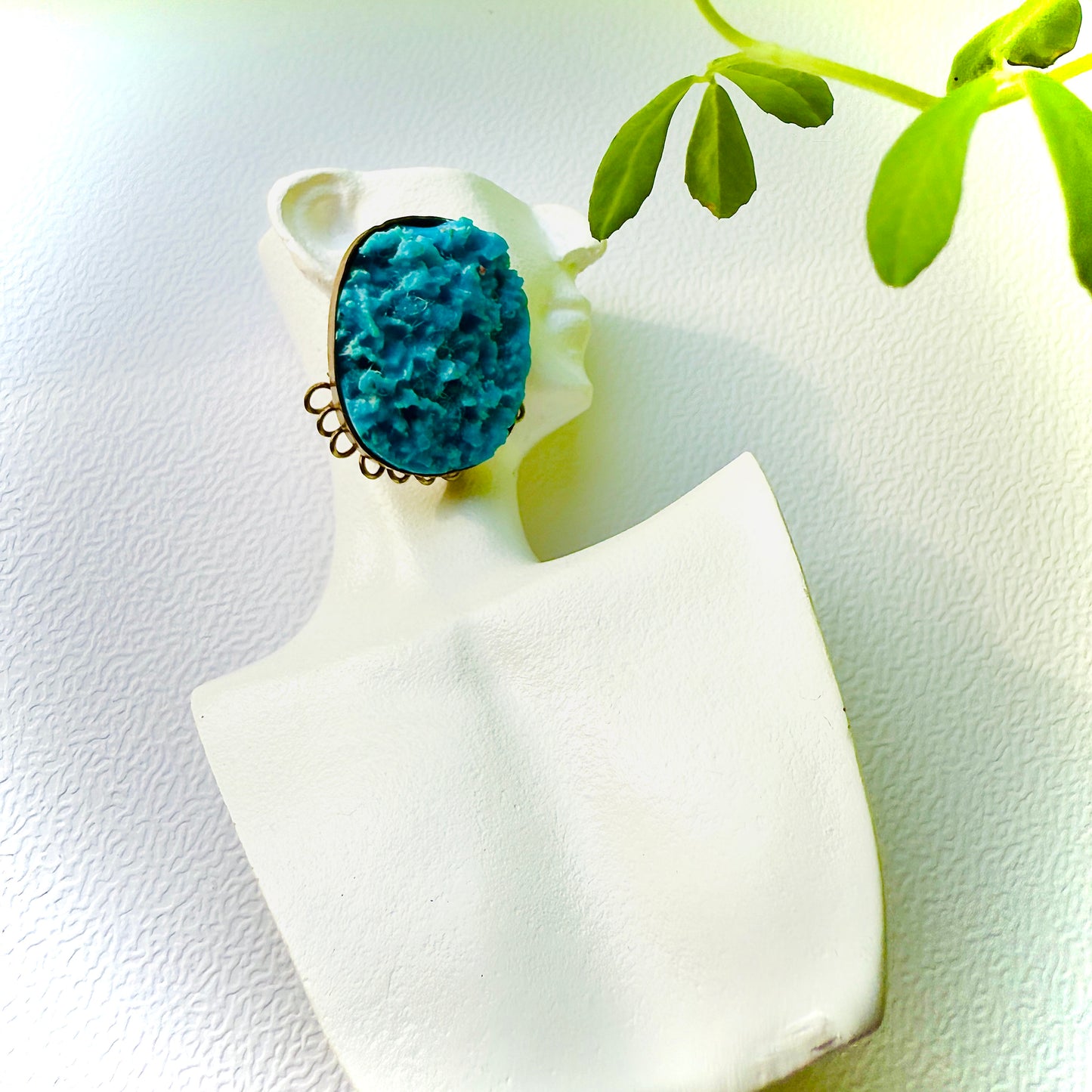 Ring with a blue stone on a white cushion with green leaves in the background