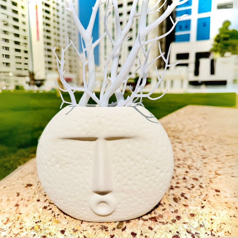 Decorative stone face with white branches on a pebble surface with blurred cityscape in the background