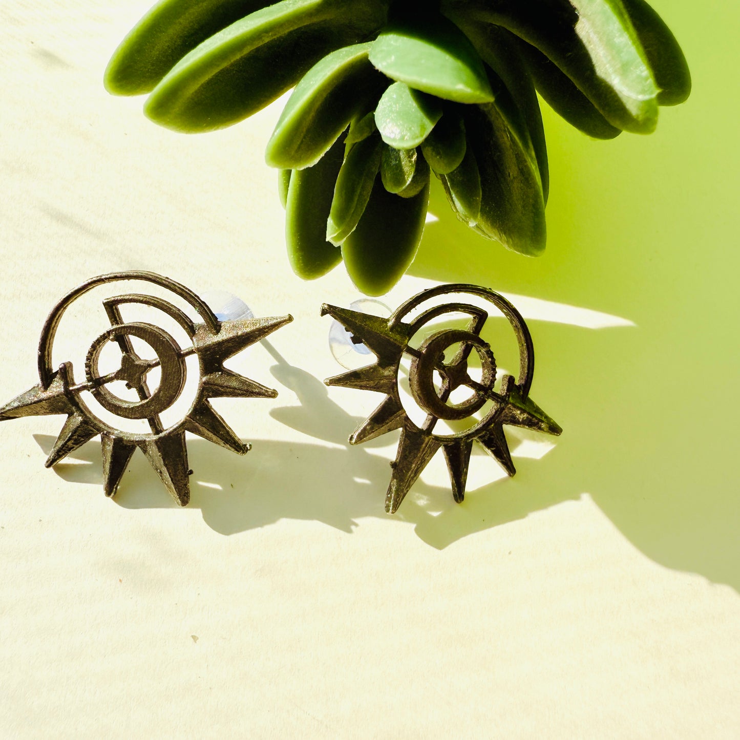 Pair of sun-shaped earrings on a light surface with green leaves in the background