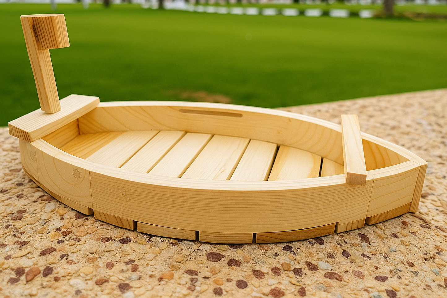 Wooden toy boat on a pebbled surface with grass in the background