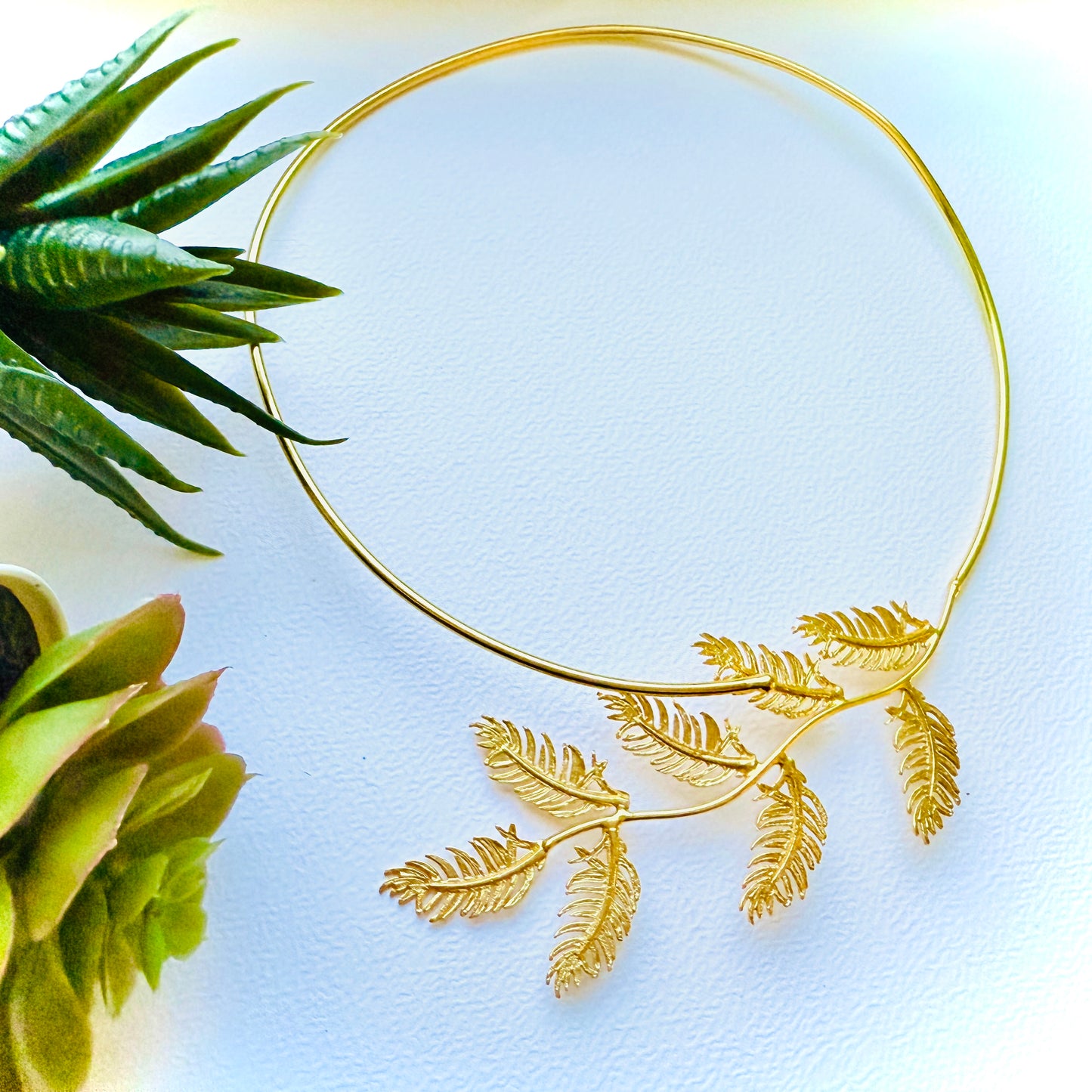 Gold leaf headband on a light blue background with green plants