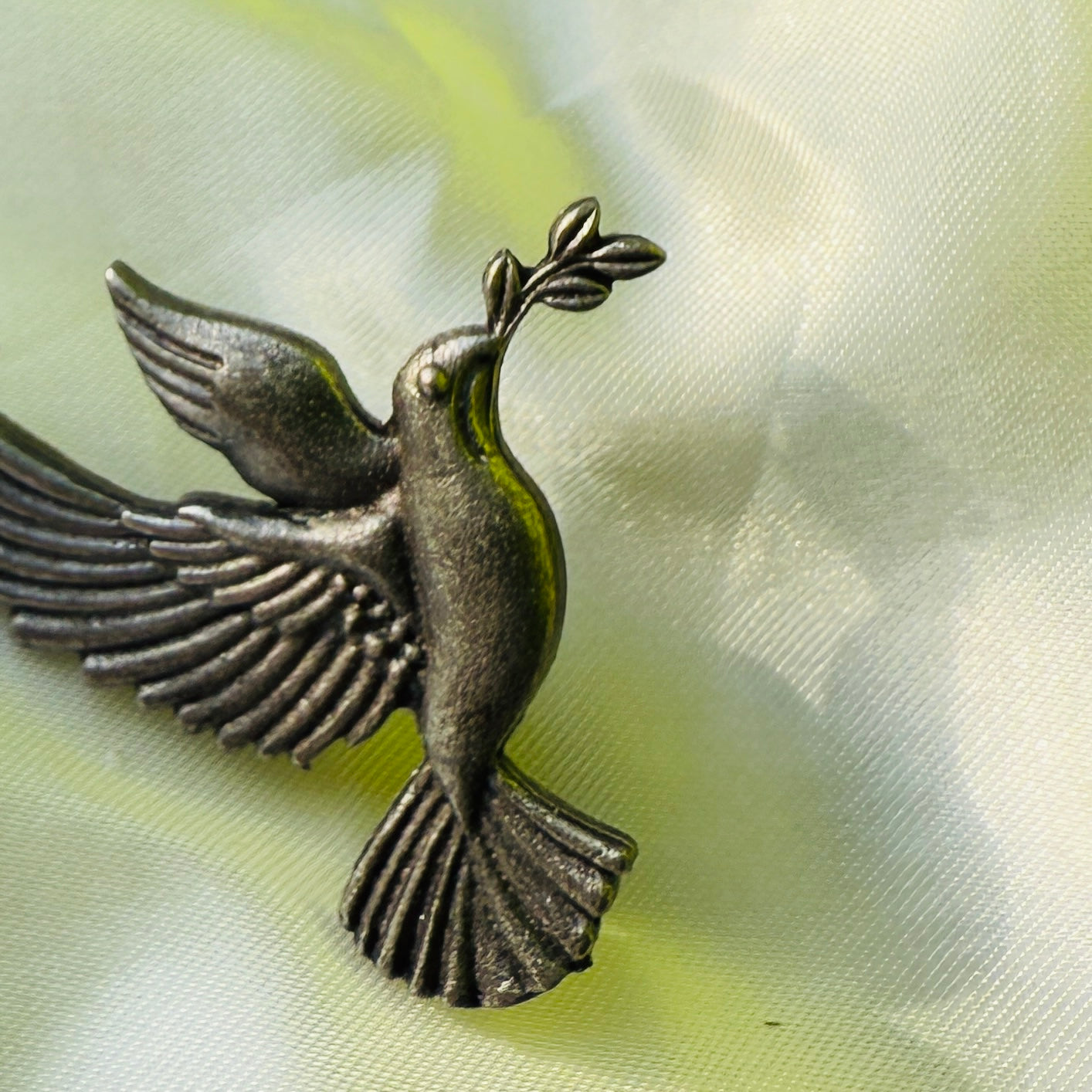 Bronze dove with olive branch on a light fabric background