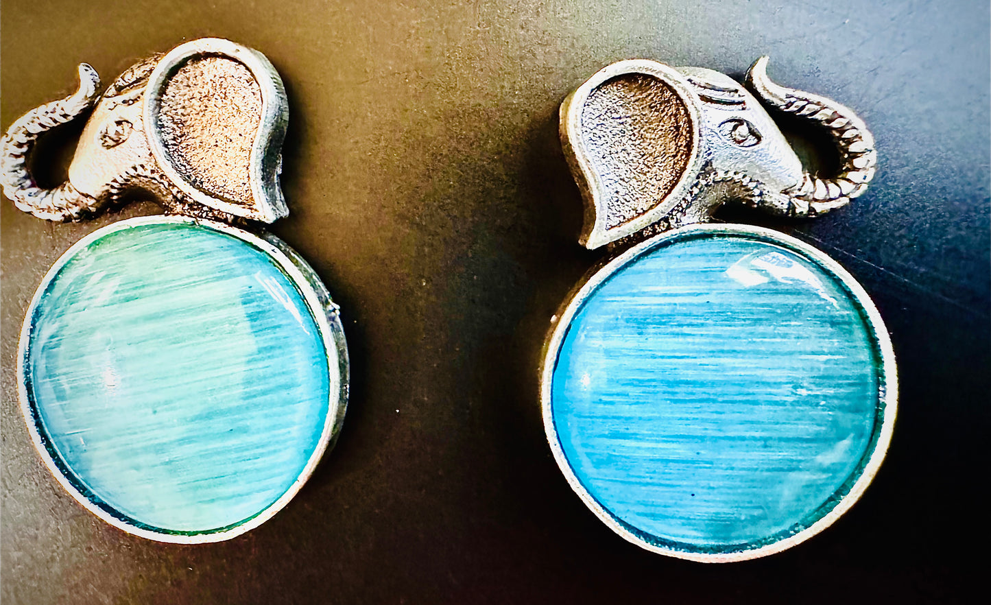 Pair of elephant-shaped earrings with blue stone centers on a dark background