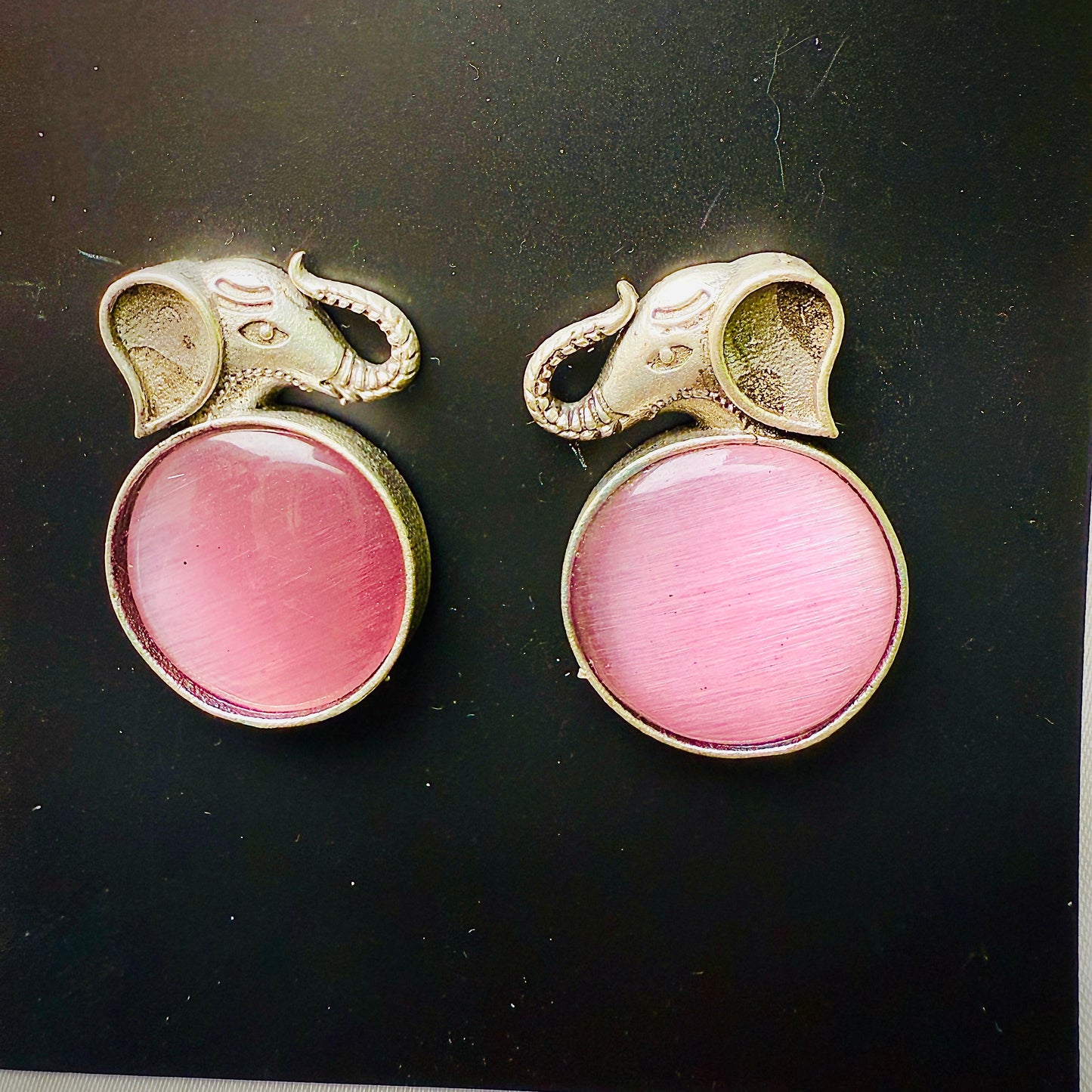 Pair of earrings with pink gemstones and gold elephant designs on a black background