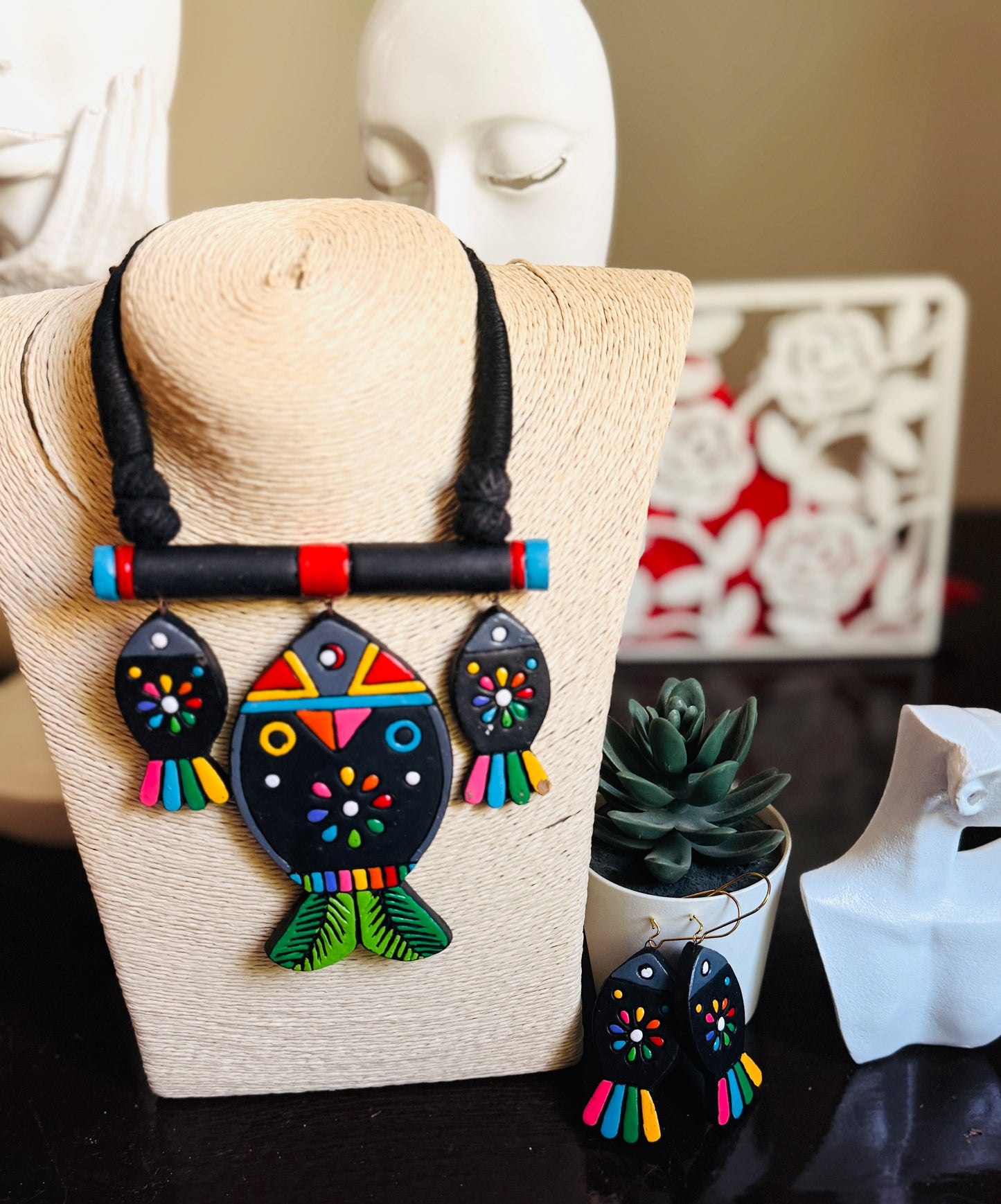 Colorful fish-shaped earrings on a mannequin bust with a blurred decorative background.