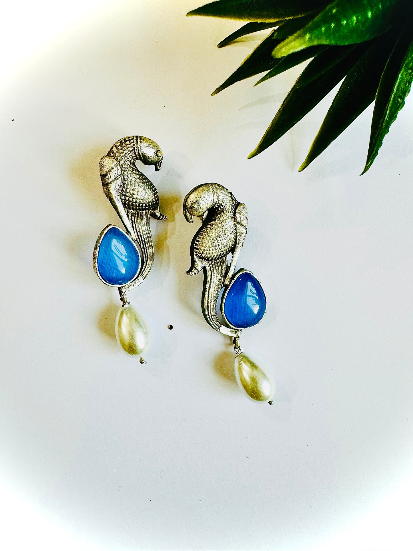 Pair of earrings with blue teardrop and pearl-like stones on a white background