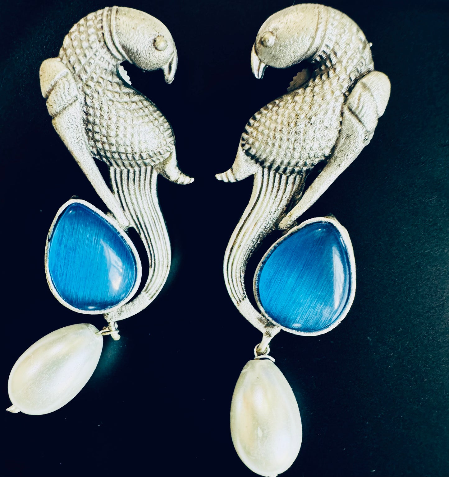 Pair of silver parrot-shaped earrings with blue stones and a pearl on a black background