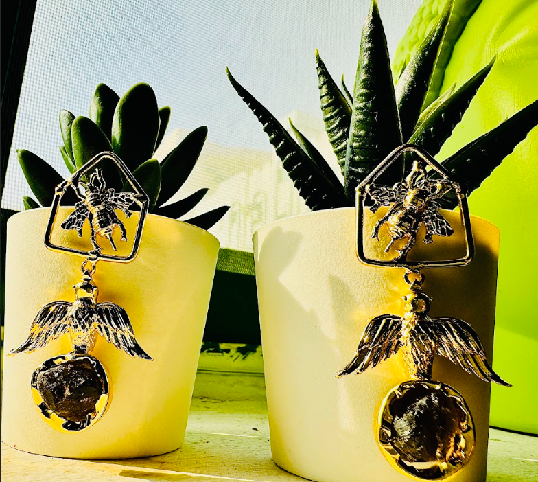 Decorative earrings with bird and ball design in front of potted plants