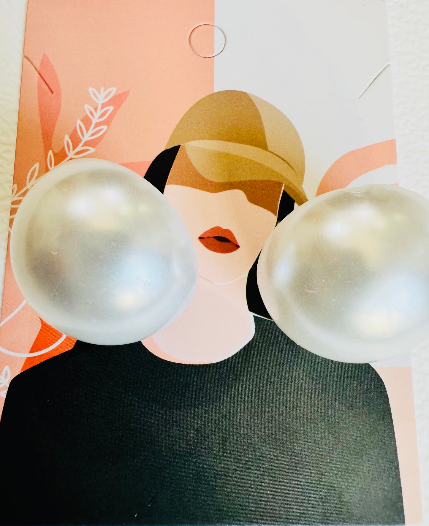 Pearl-like spherical earrings on a card with a stylized face design.