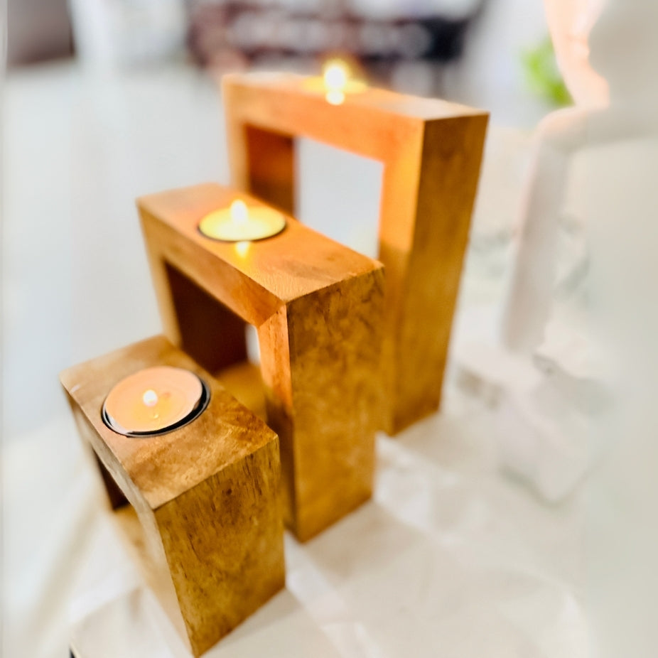 Three wooden candle holders with candles on a white surface