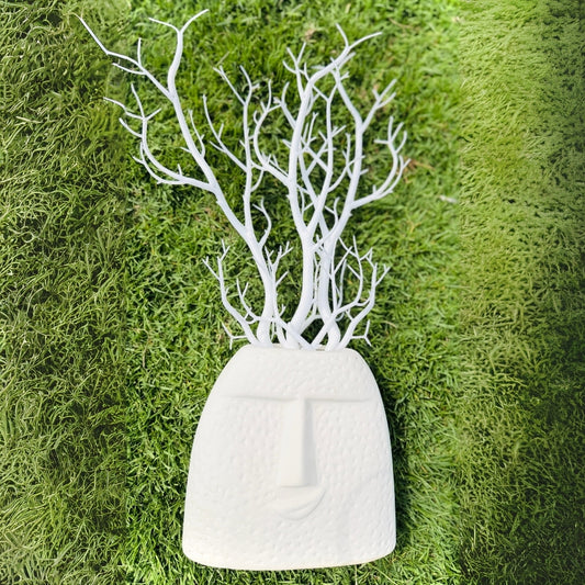 White decorative vase with branch-like structure on a green moss background