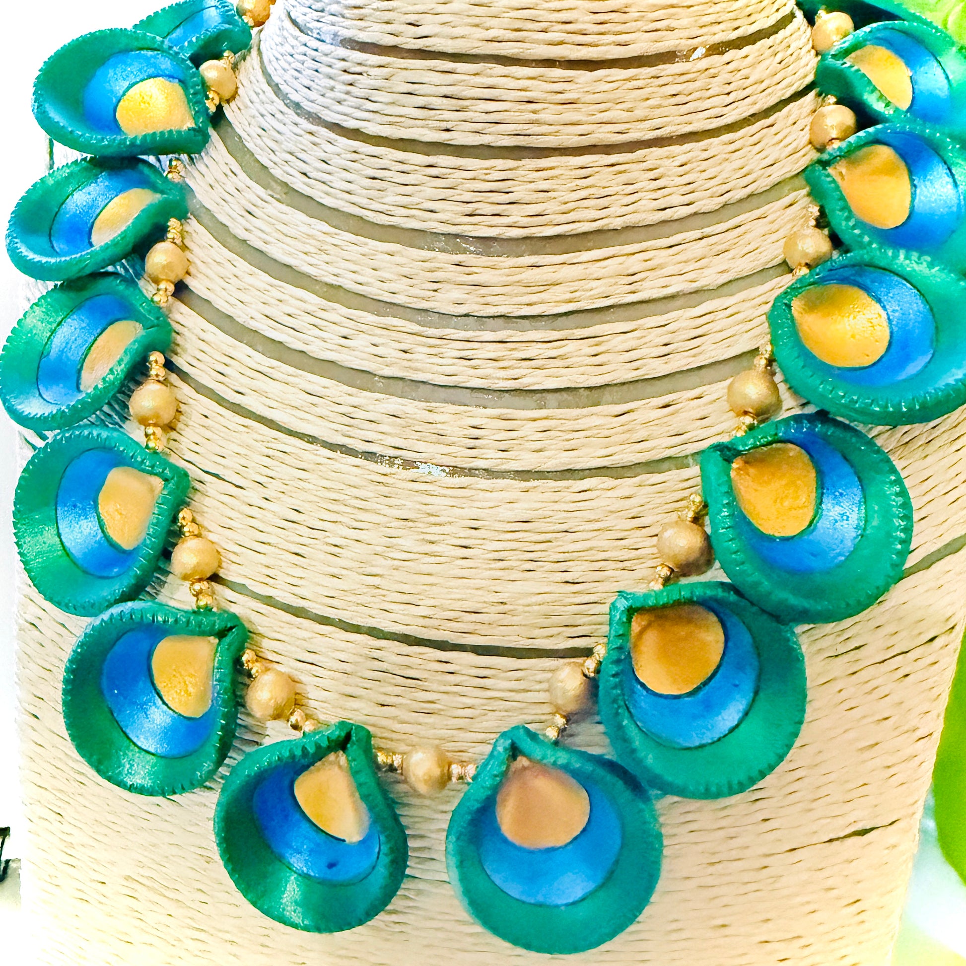 Necklace with green and blue peacock feather-like pendants on a woven surface