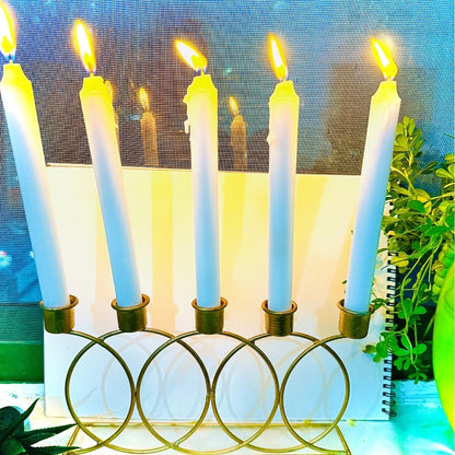 Candle holder with lit candles on a table with a plant and notebook in the background