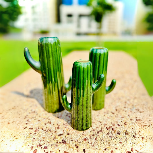 Three green cactus-shaped objects on a sandy surface with a blurred outdoor background.