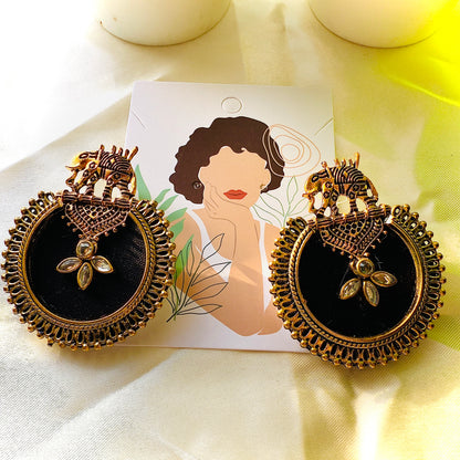 Ornate earrings with black center and gold detailing on a white card with a woman's face.