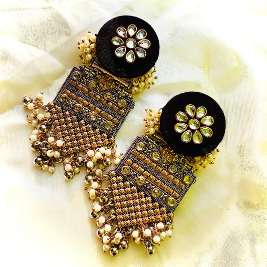 Ornate earrings with black and gold details on a light fabric background