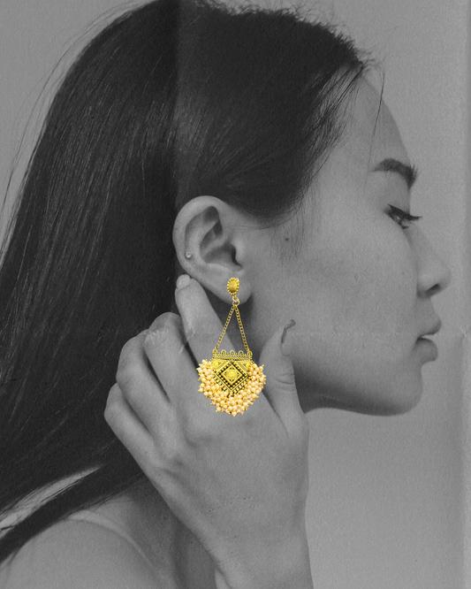 Gold earring worn by a person with a gray background