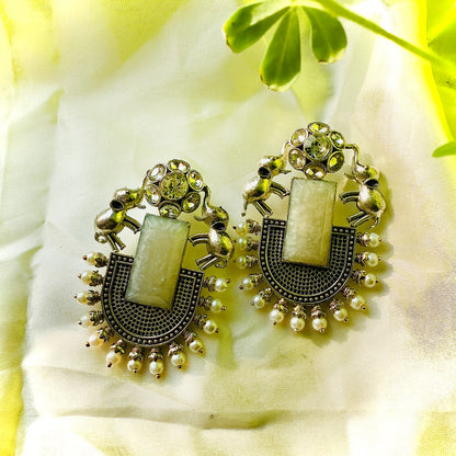 Pair of ornate earrings with green stones on a light fabric background