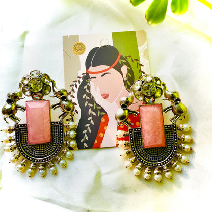 Decorative earrings with pink center and gold accents on a white surface with a decorative card.