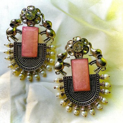 Ornate earrings with pink central stones and pearl accents on a light fabric background