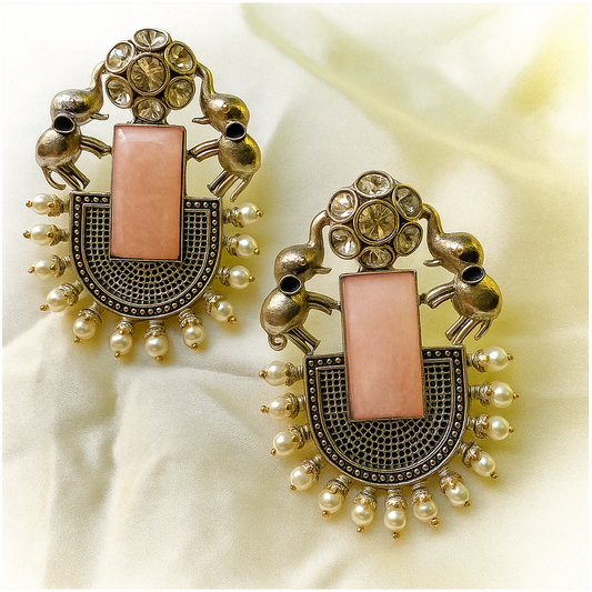 Ornate earrings with pink central stone and gold accents on a light fabric background