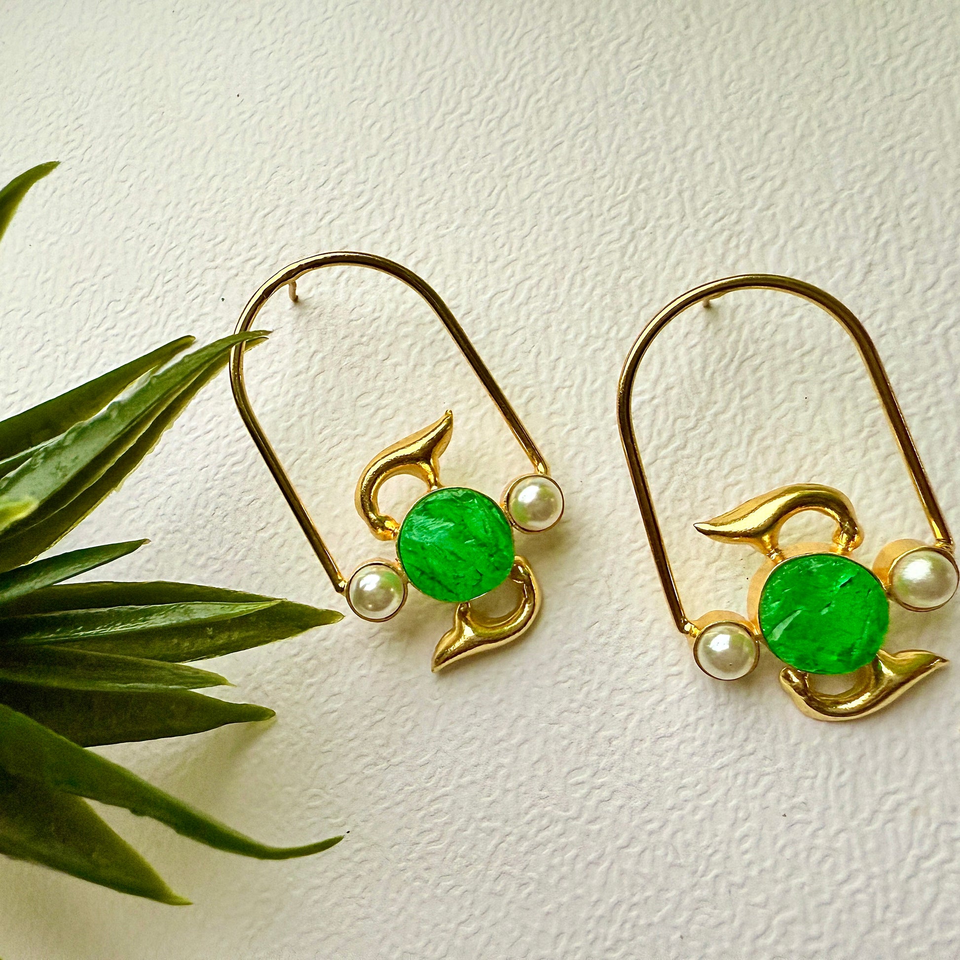 Gold earrings with green gemstones and pearls on a light background