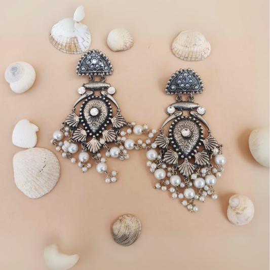 Ornate silver earrings with pearls on a beige background with seashells