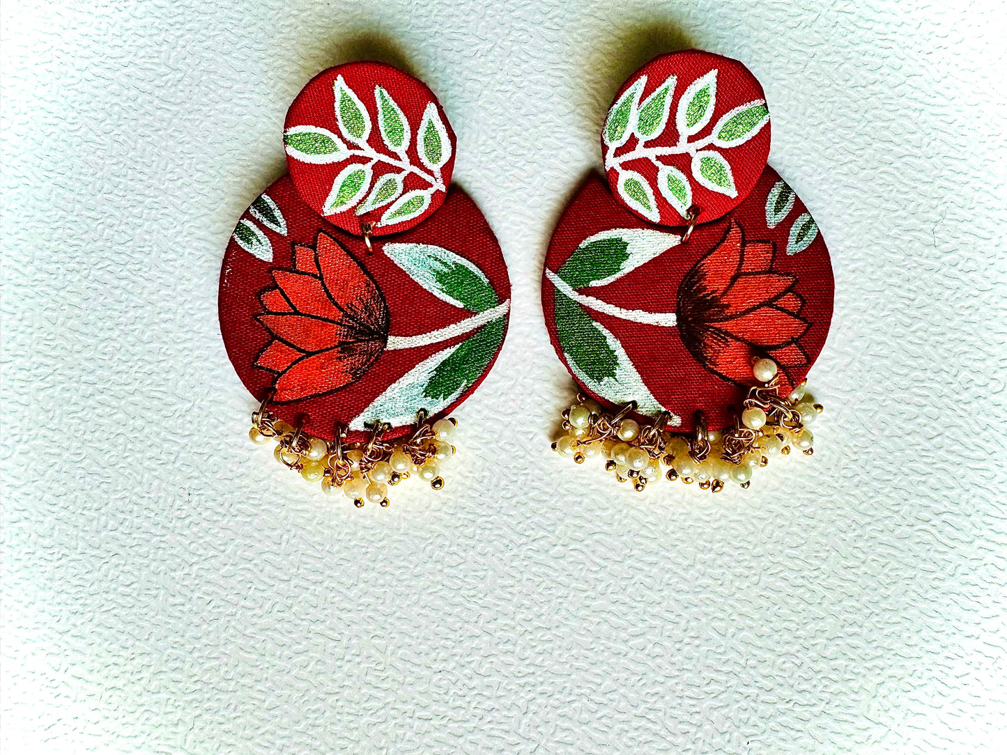 Pair of red floral earrings with green leaves on a light gray background