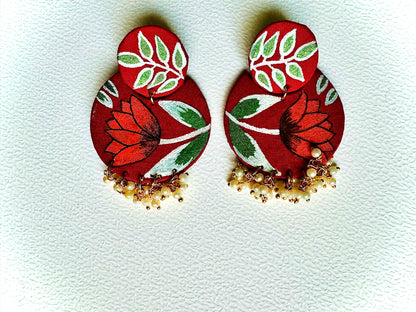 Pair of red floral earrings with green leaves on a light gray background