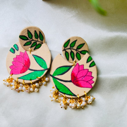 Pair of wooden earrings with floral designs and pearl-like beads on a light background