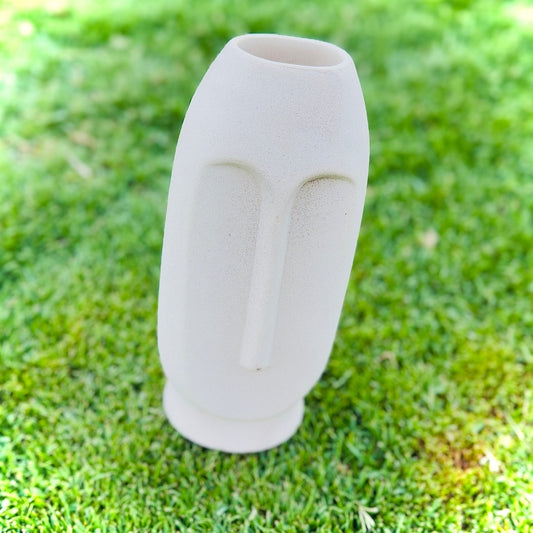 White ceramic vase with a face design on grass