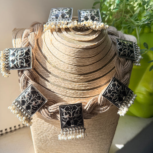 Decorative headpiece with black square ornaments and white beads on a mannequin head.